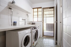 A laundry area with a washing machine and dryer, a countertop with a soap dispenser, and a window with blinds.