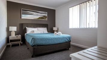 A neatly arranged hotel room with a bed, two bedside tables, a window with blinds, and a painting on the wall.