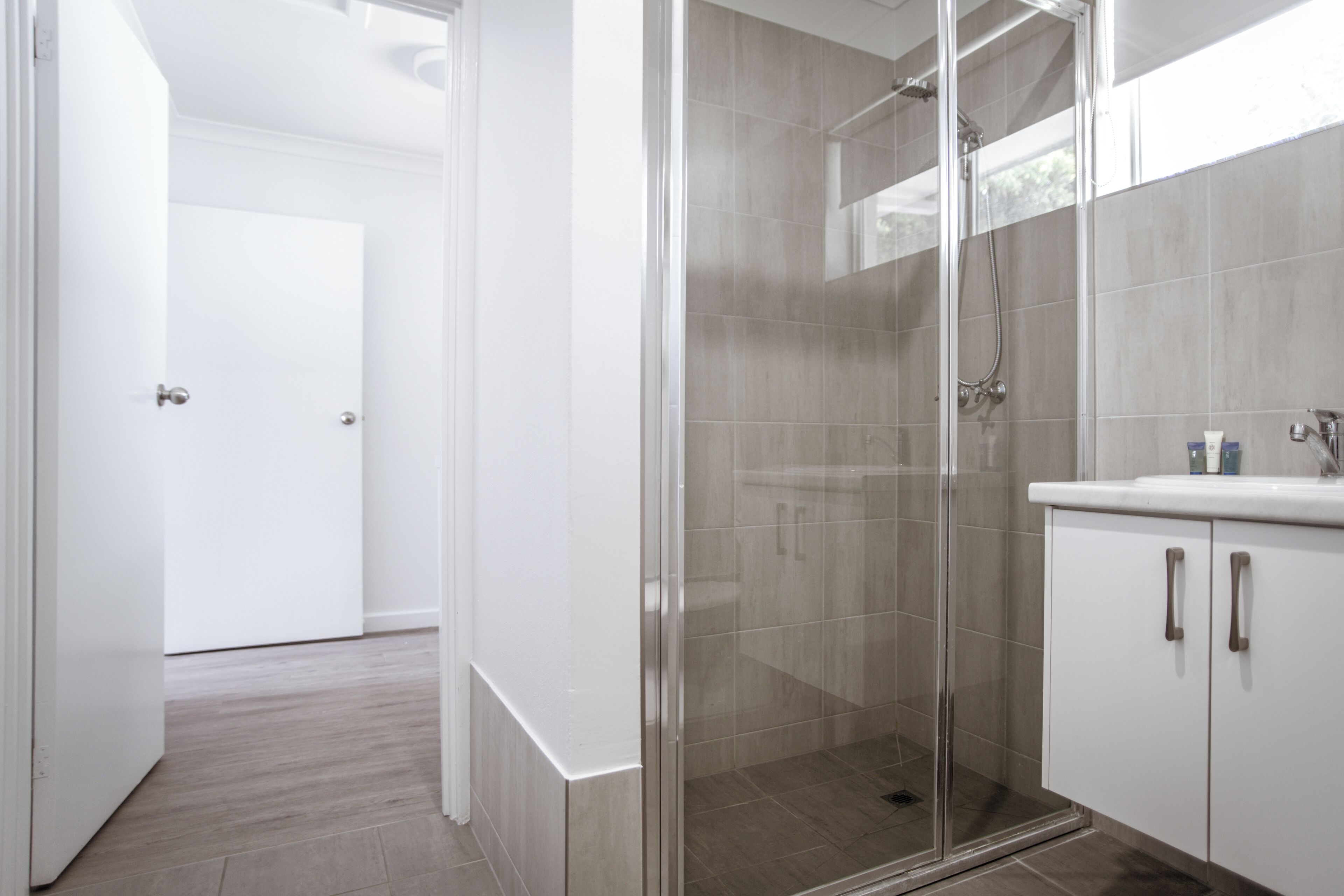 Un baño moderno con cabina de ducha de vidrio, muebles de tocador blancos y suelo de baldosas.