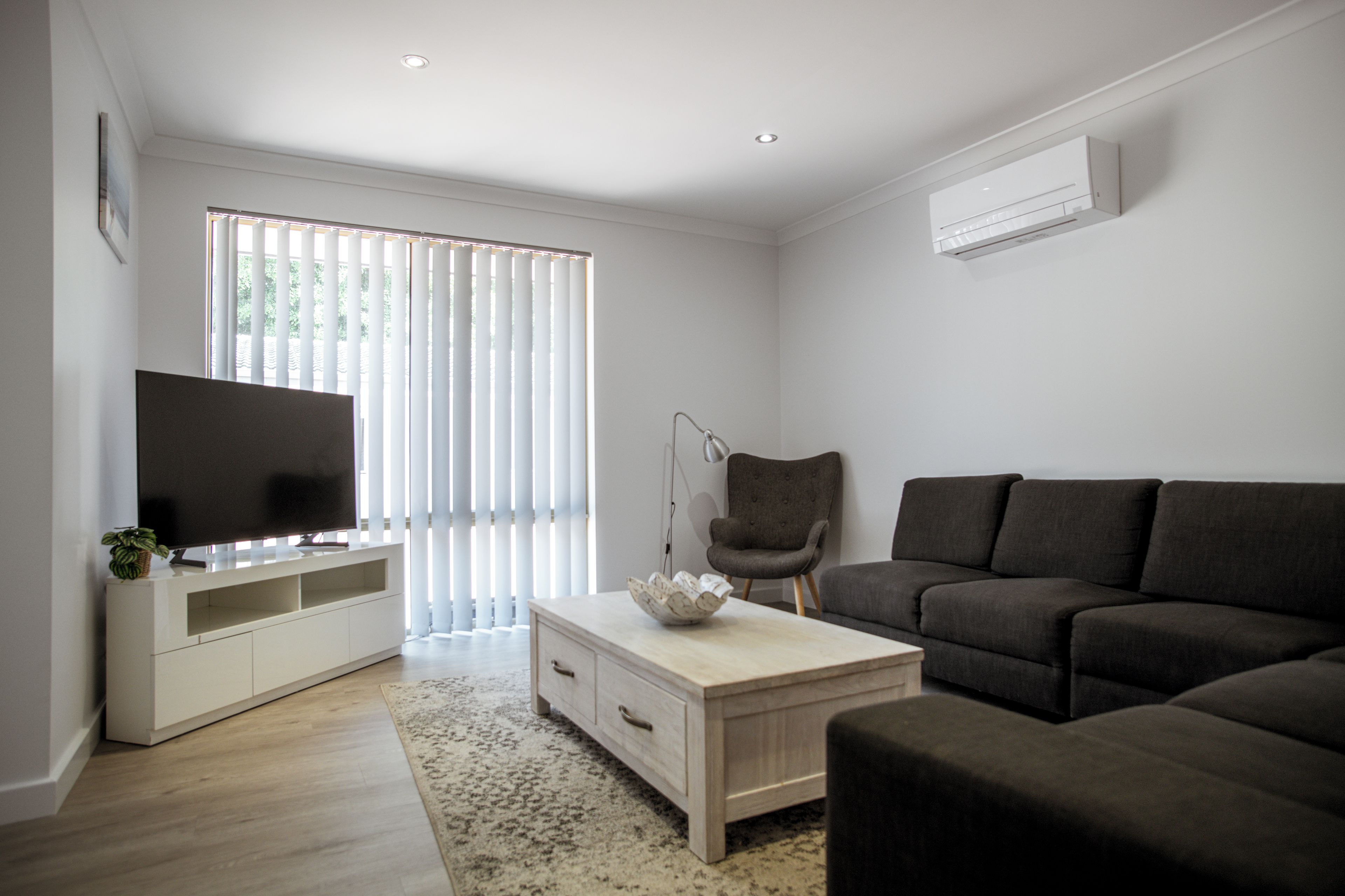 A modern living room with a flat-screen TV, a grey sofa, a white coffee table, and a grey armchair.