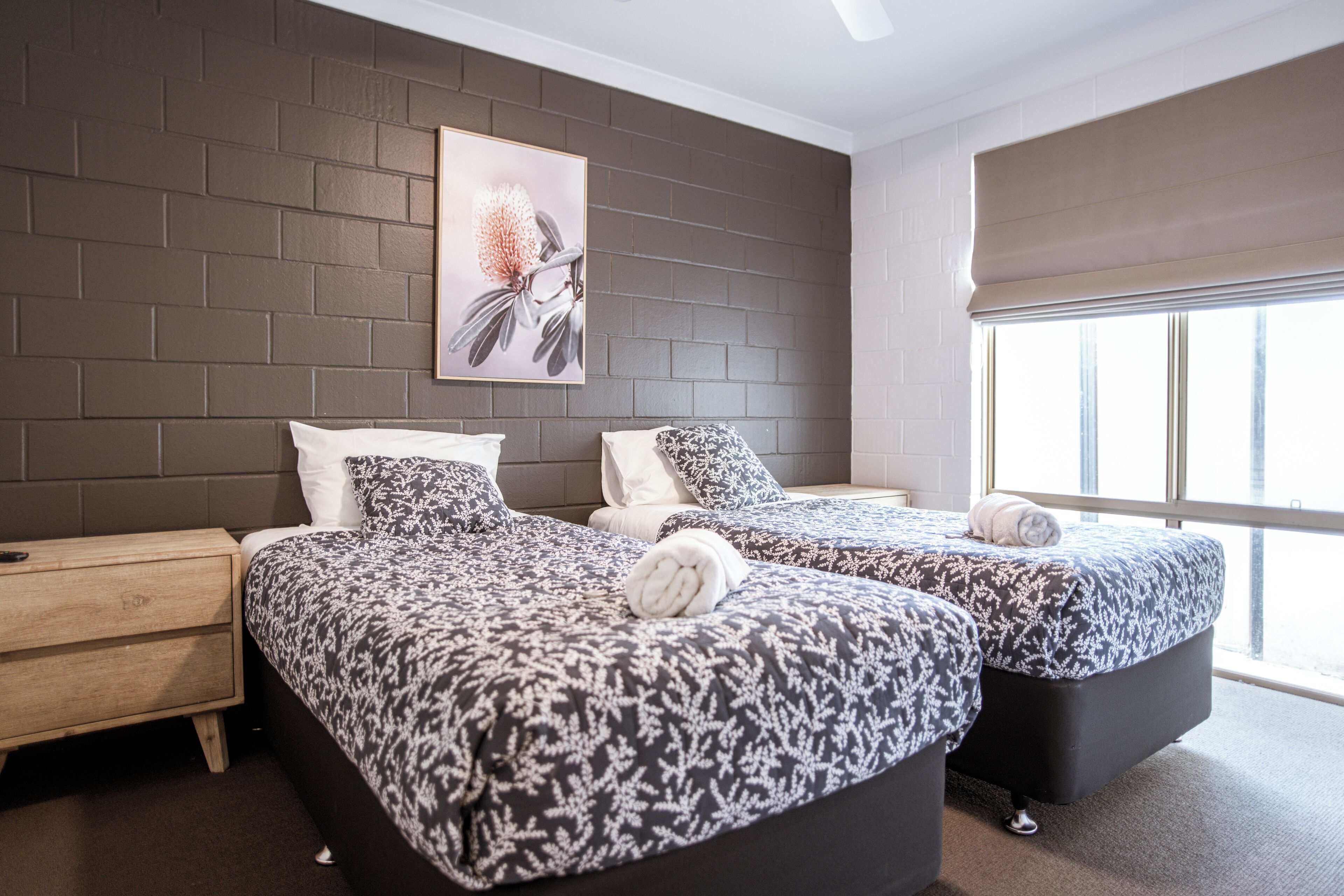 A modern hotel room with two beds, a large window, and a brick wall.