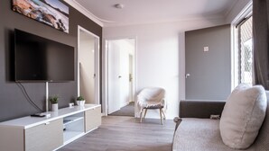 Una sala de estar moderna con una televisión de pantalla plana, un sofá, una silla y una consola con plantas.