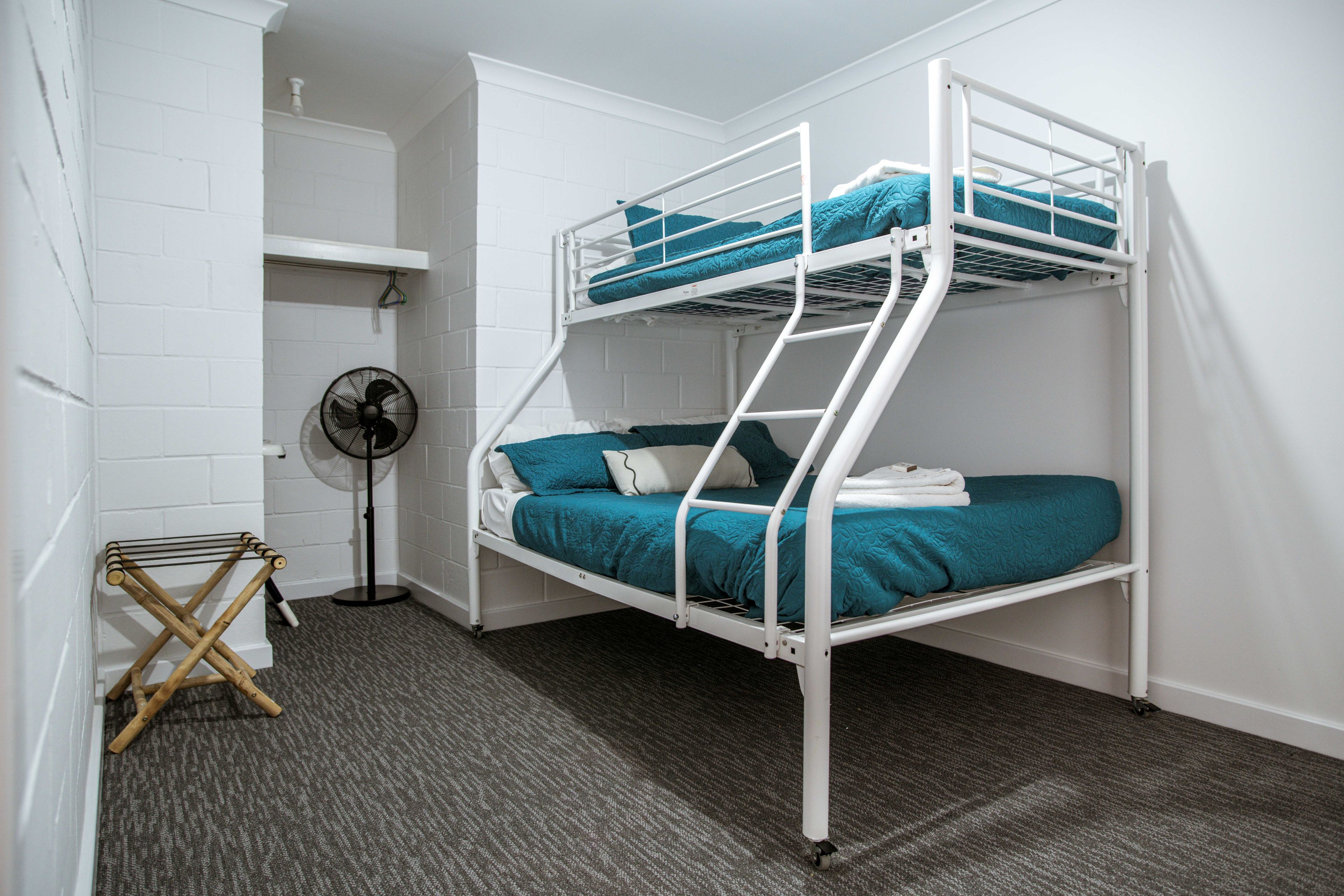 A bunk bed with a fan and a drying rack in a room with white brick walls.