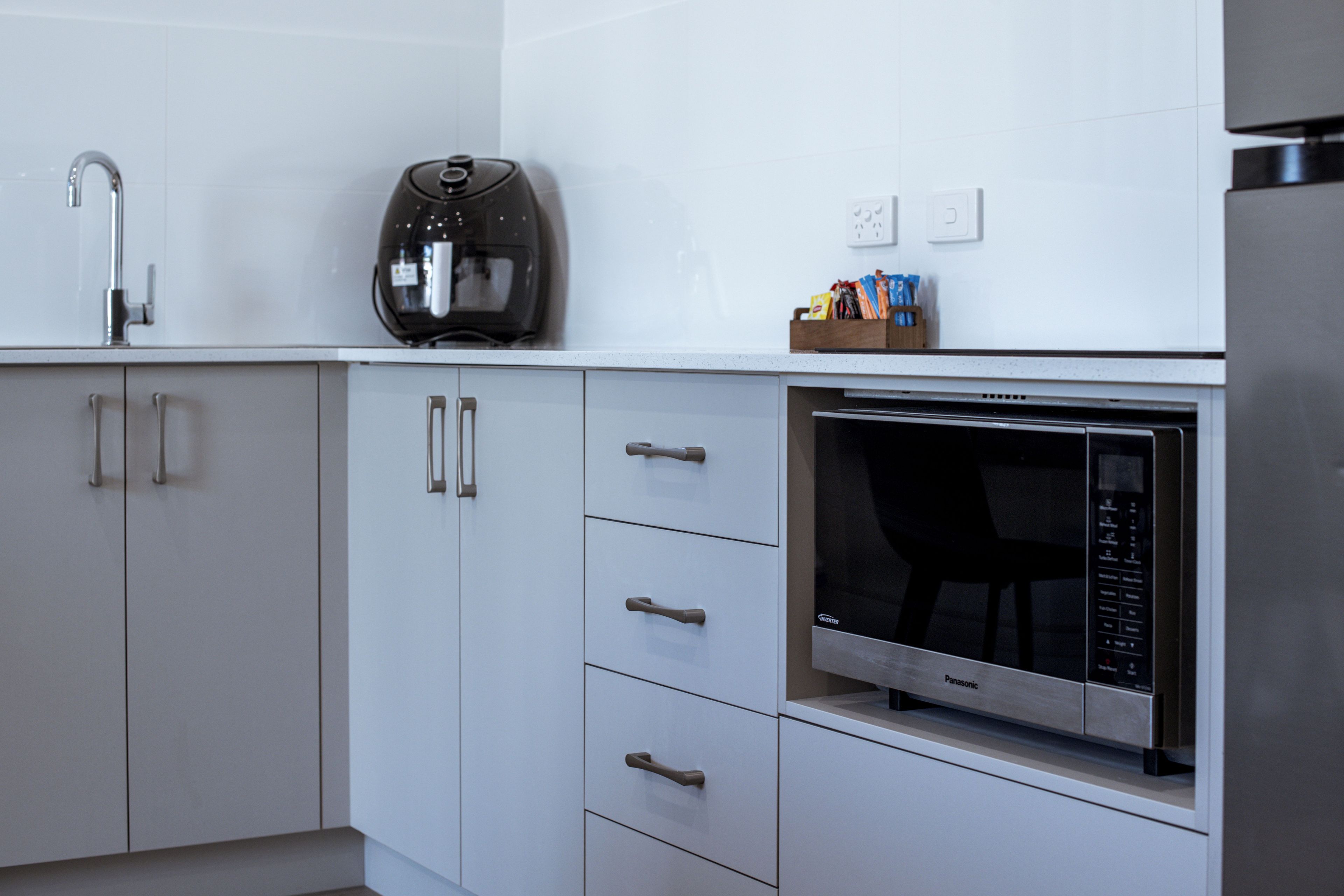 Una cucina moderna con mobili bianchi, forno a microonde integrato e macchina da caffè.