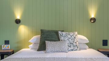 A neatly made bed with patterned bedding and pillows, two wall-mounted light fixtures, and a small table with a colorful item on it.