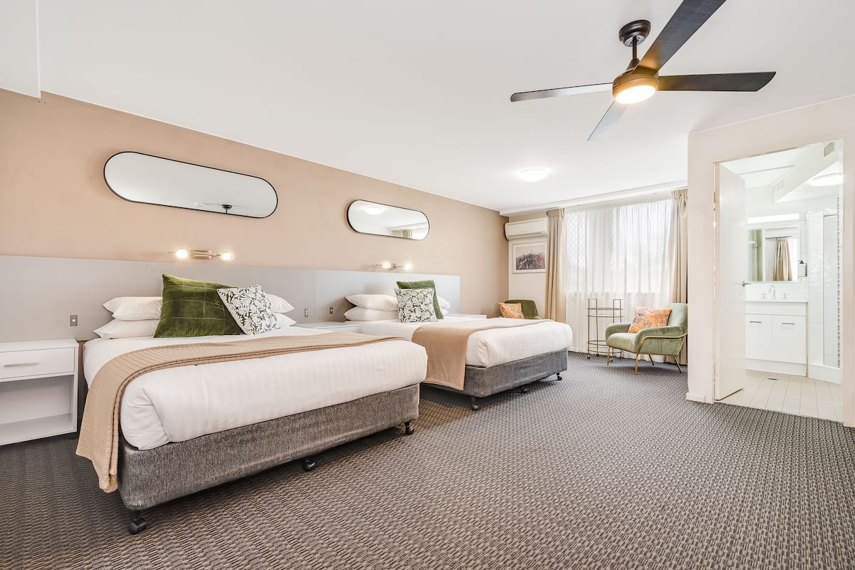 Habitación de hotel con dos camas, un ventilador de techo y un baño visible a través de una puerta abierta.
