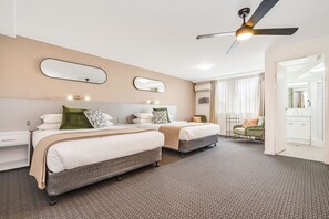 Een hotelkamer met twee bedden, een plafondventilator en een zichtbare badkamer door een open deur.