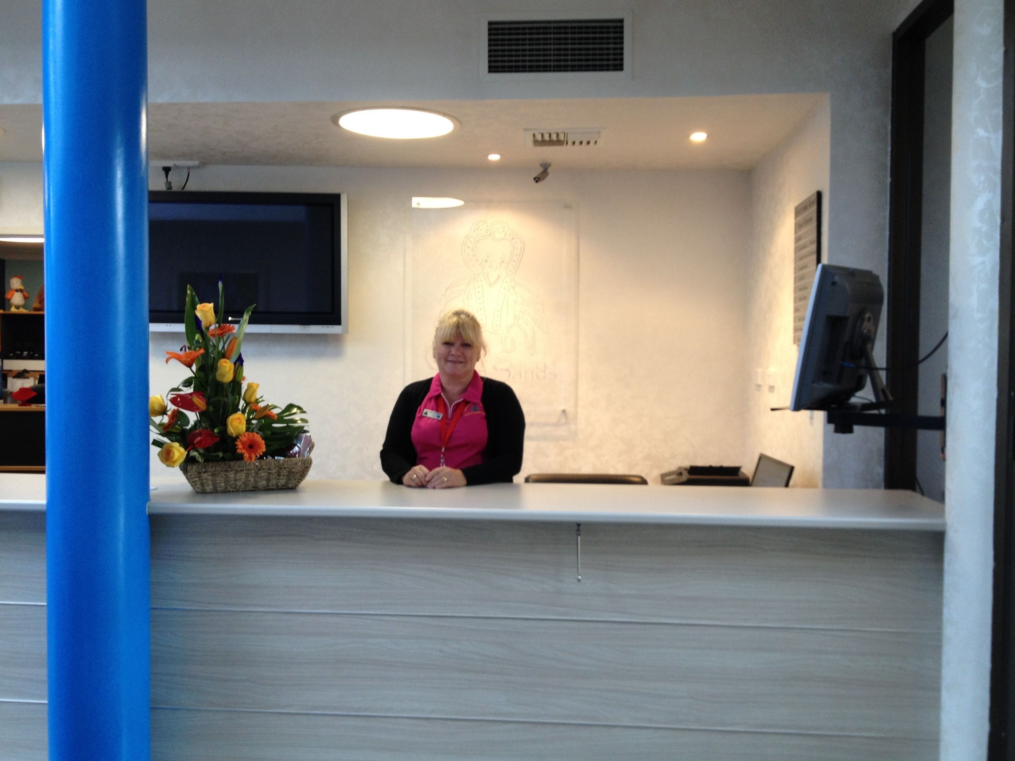A reception area with a flat-screen TV mounted on the wall, a basket of flowers, and a desk with a computer monitor.