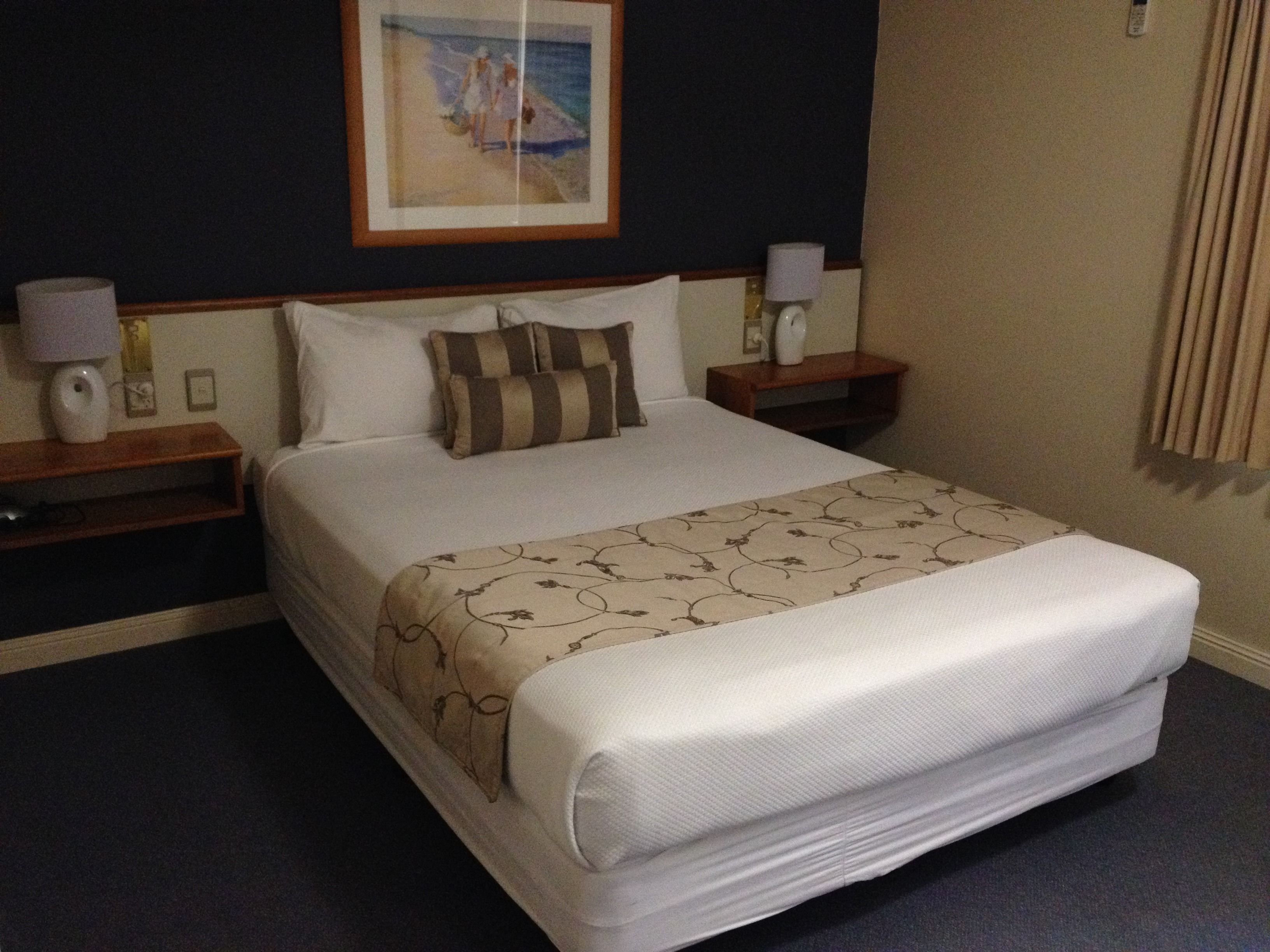 A hotel room with a large bed, two bedside tables, a nightstand, a lamp, and a framed picture on the wall.