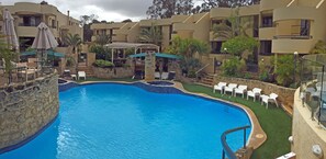 A swimming pool surrounded by lounge chairs and umbrellas, with a stone wall and greenery. - Silver Sands Resort (Silver Sands)