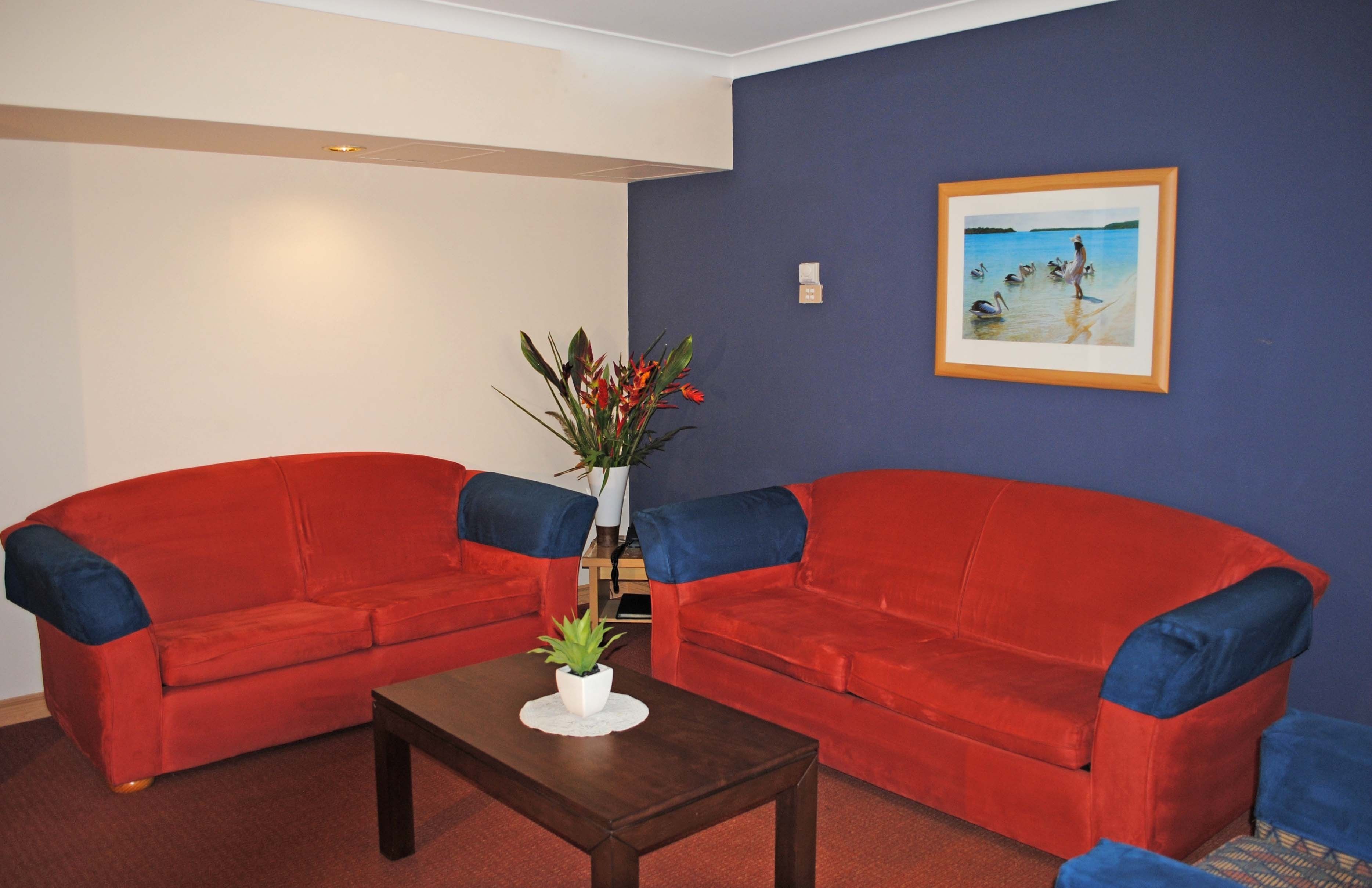 A living room with two red sofas, a small coffee table with a plant, and a framed picture on the wall.