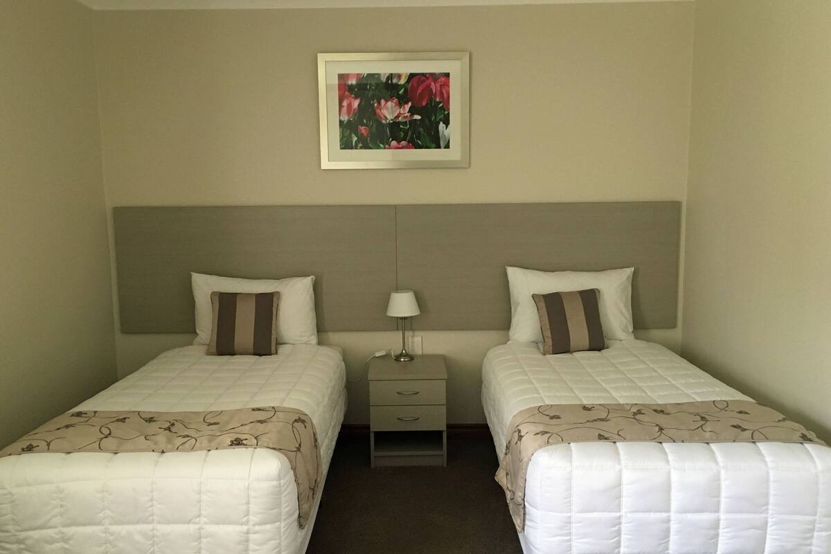 A hotel room with two beds, each with a pillow and a bedside table with a lamp.