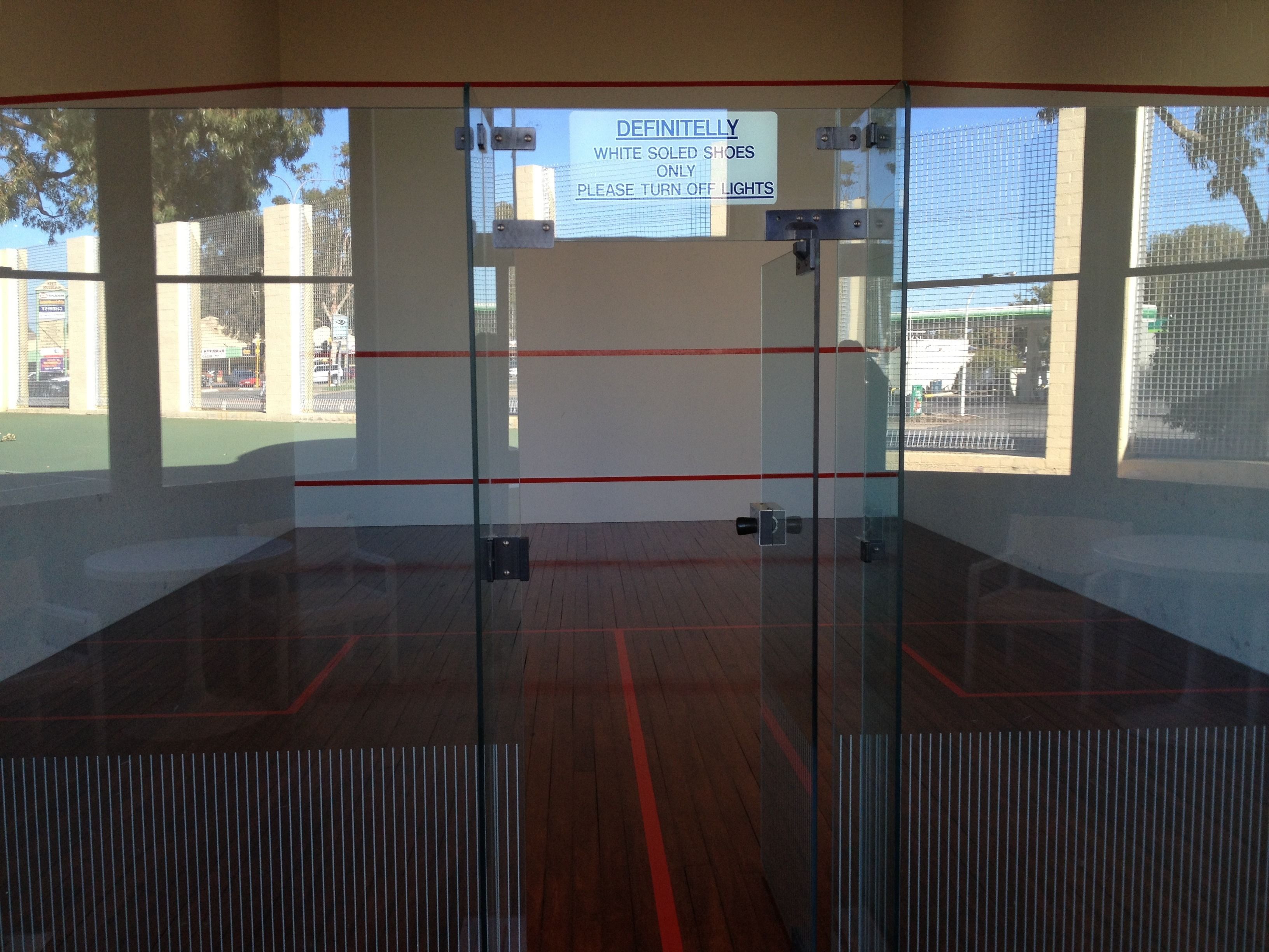 A squash court with a sign indicating white-soled shoes only and to turn off lights.