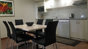 Una cocina moderna con armarios blancos, un microondas y un hervidor. Hay una mesa de comedor con sillas negras y un cuenco negro encima.