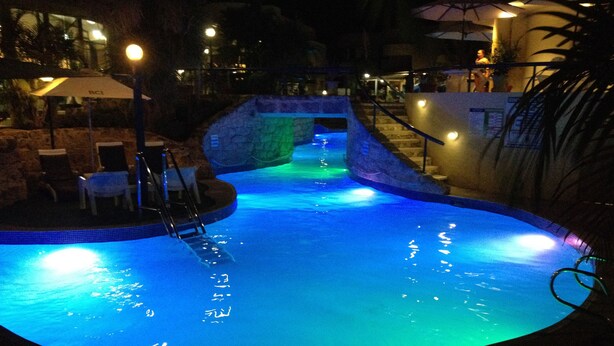 Una piscina con un muro de piedra y escalones que bajan a ella, rodeada de mobiliario exterior e iluminación.