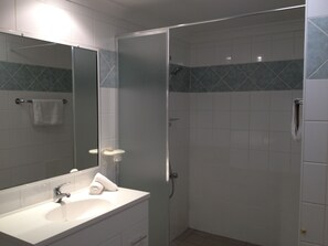 A bathroom with a white sink, a mirror, and a shower with a glass door. - Silver Sands Resort (Silver Sands)