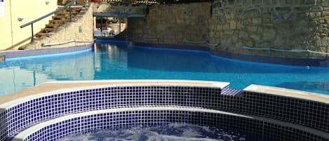 A swimming pool with a stone wall and a staircase leading up to a building.