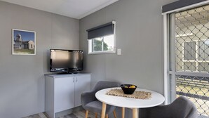 Un espacio habitable compacto con kitchenette, televisor, zona de comedor con dos sillas y ventana con vistas.