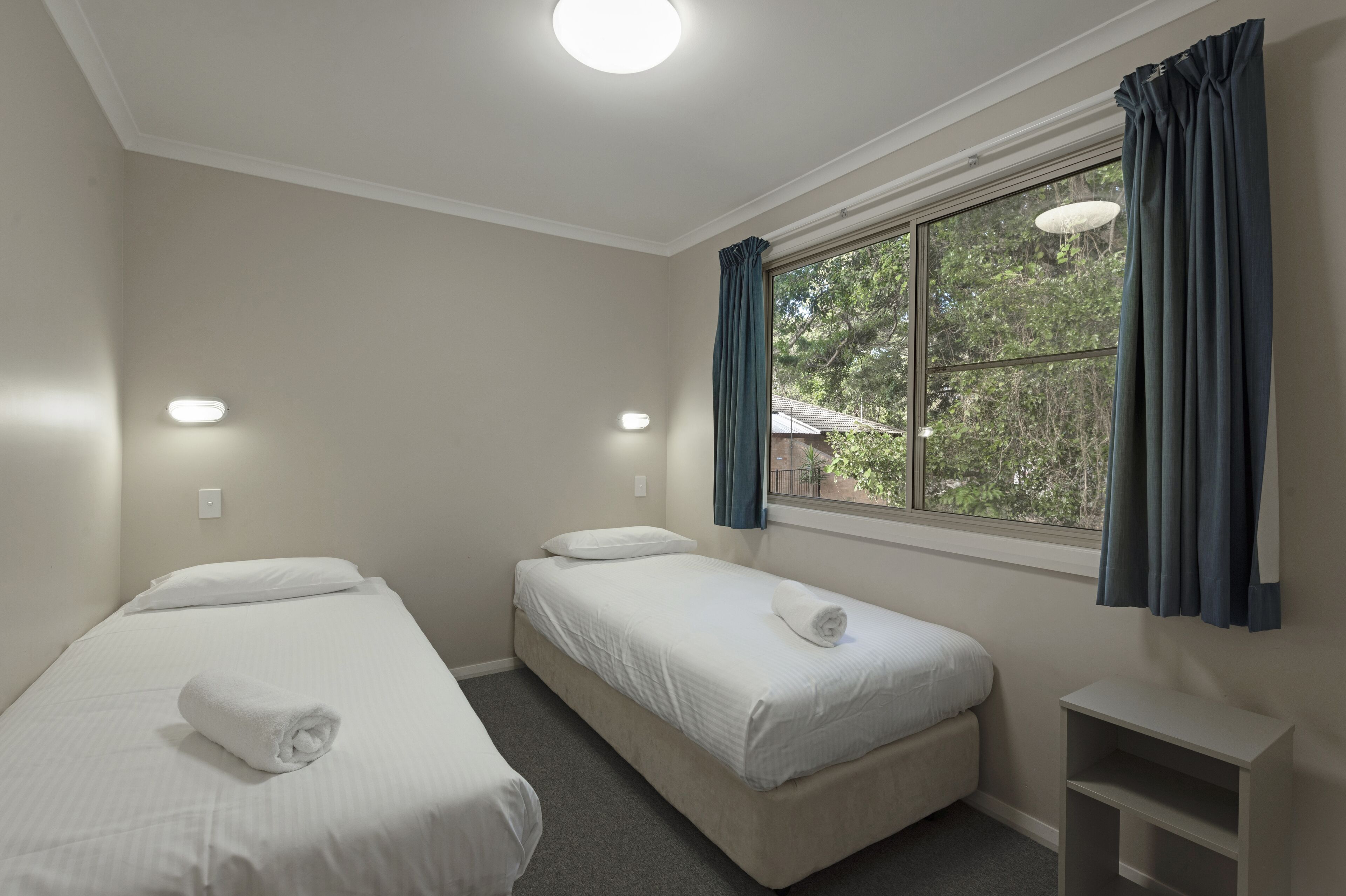 A room with two single beds, a small table, and a window with curtains.