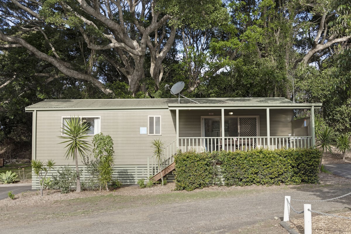 Ein Bungalow mit Veranda, Satellitenschüssel und einem kleinen Garten mit verschiedenen Pflanzen.