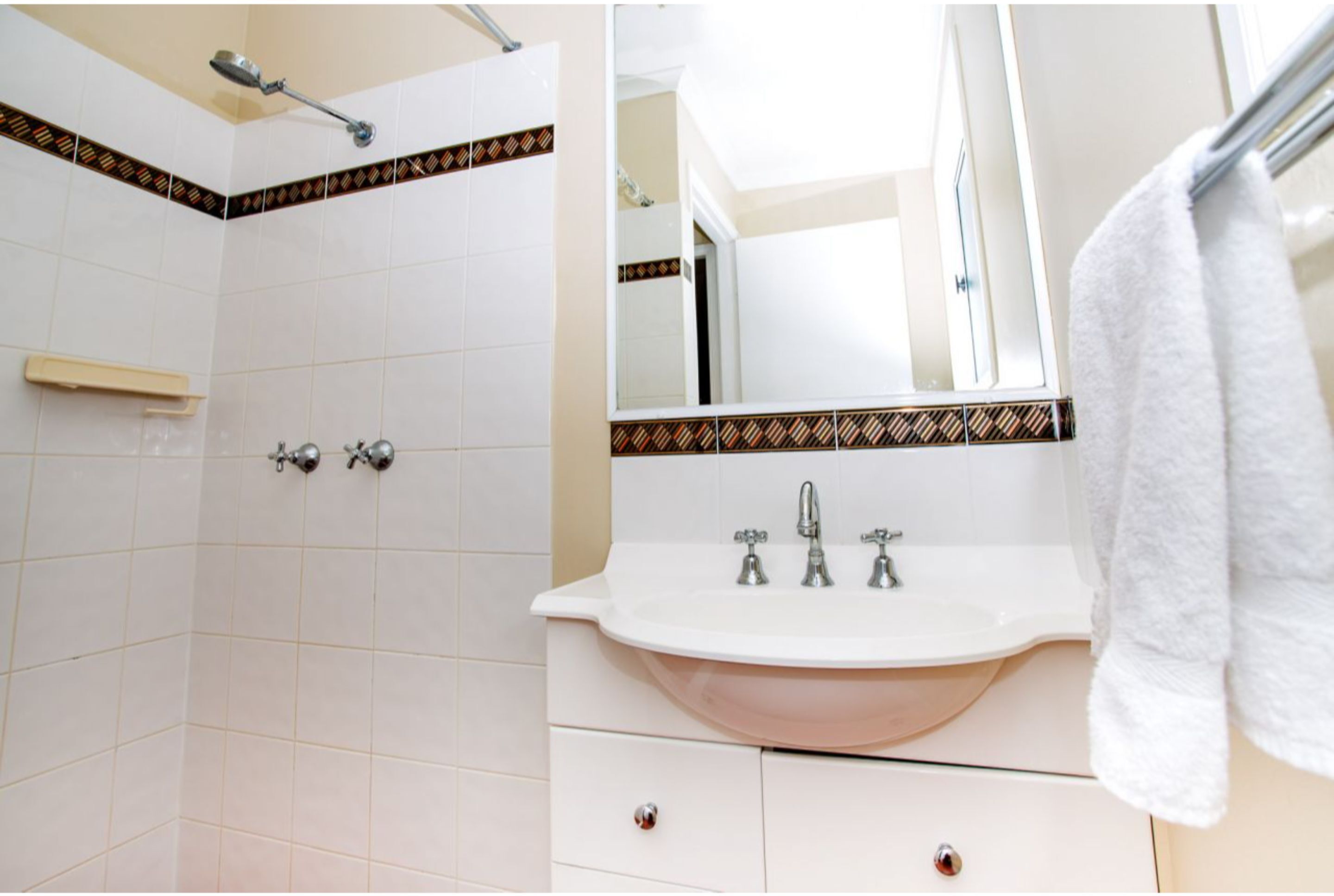 Un baño con azulejos blancos, una ducha, un lavabo con espejo y un perchero para toallas.