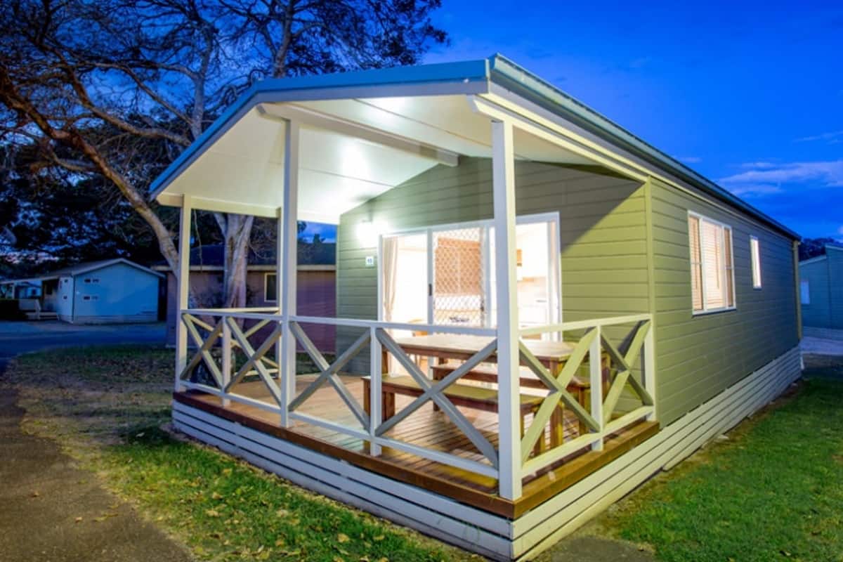 Ein kleines, eingeschossiges Mobilheim mit Veranda und einem eingezäunten Garten.