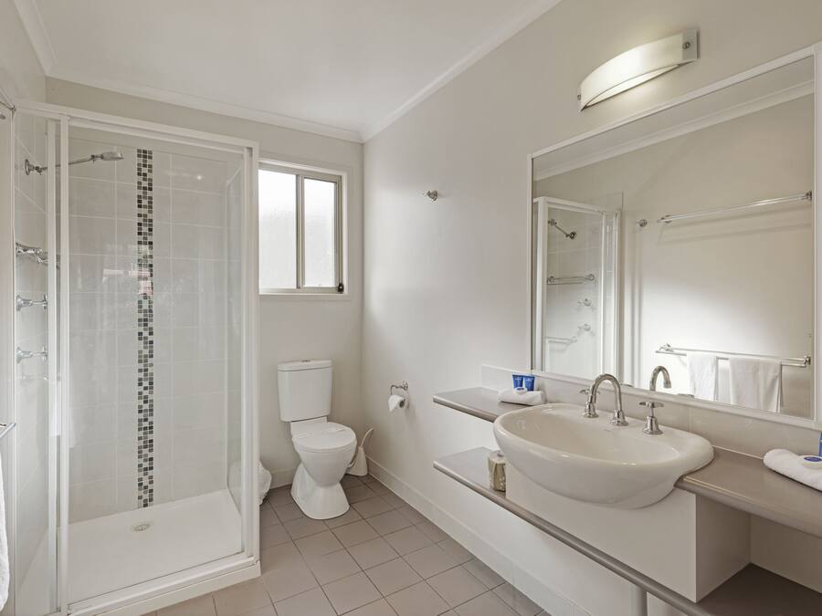 A modern bathroom with a glass-enclosed shower, a toilet, a sink, and a large mirror.