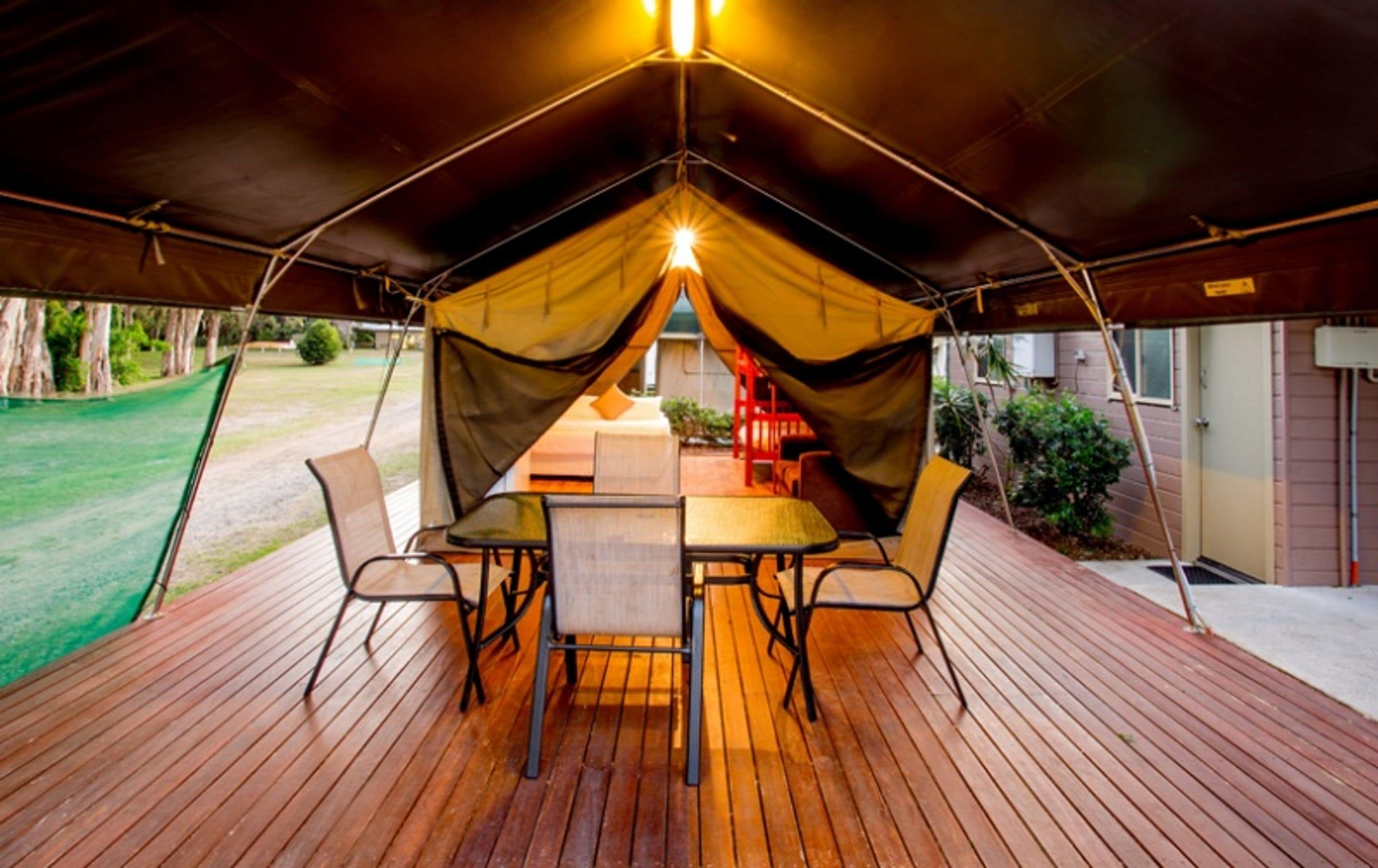 Un área de comedor al aire libre, cubierta, con una mesa y sillas, una carpa encima y vista a una casa y jardín.