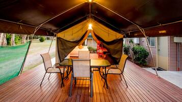 Un área de comedor al aire libre, cubierta, con una mesa y sillas, una carpa encima y vista a una casa y jardín.