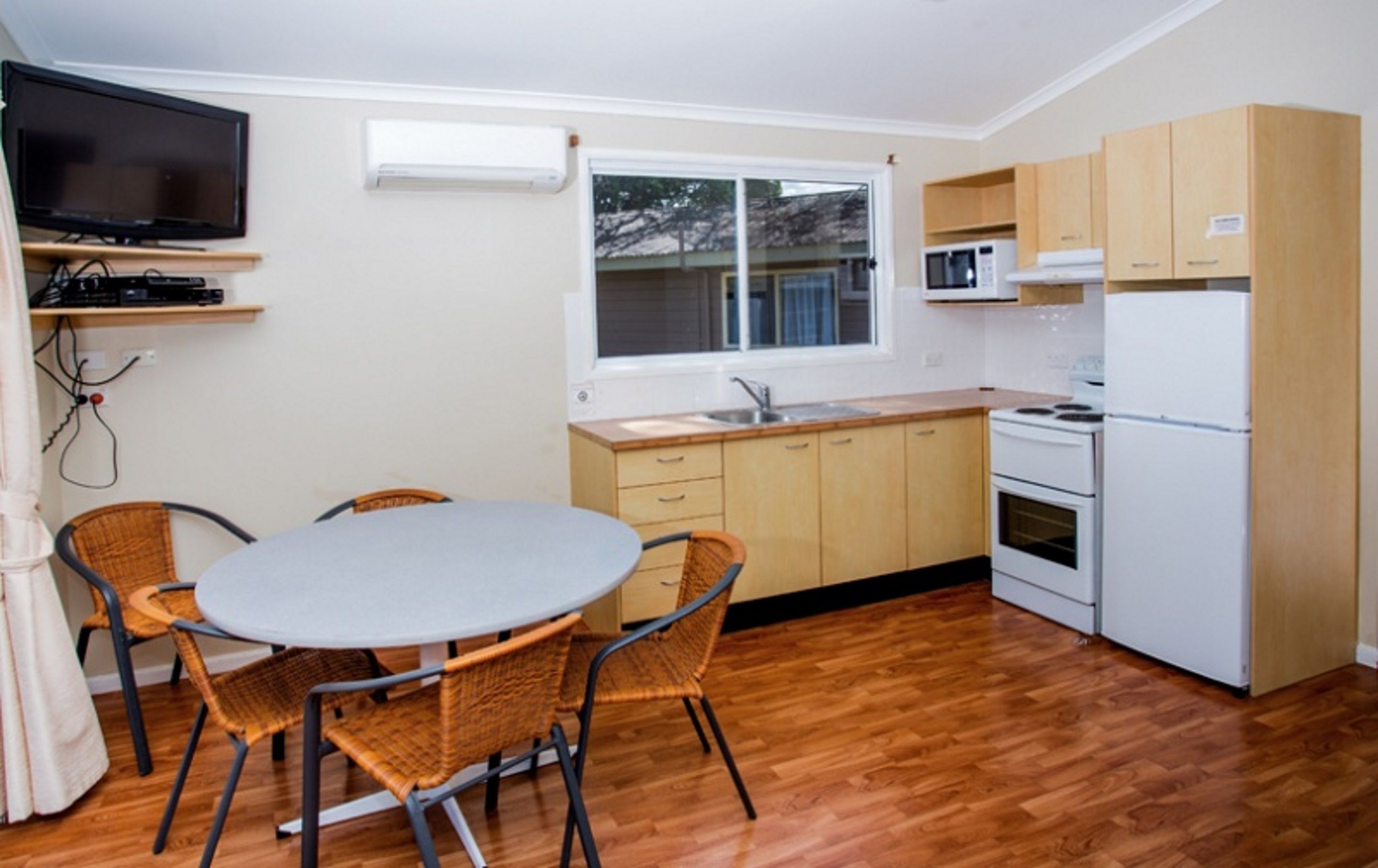 A compact kitchen with a dining area, featuring a TV, microwave, stove, and wooden cabinets.