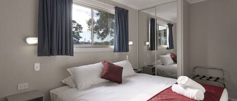 A hotel room with a bed, a ceiling fan, a window with curtains, a bedside table, and a mirror.