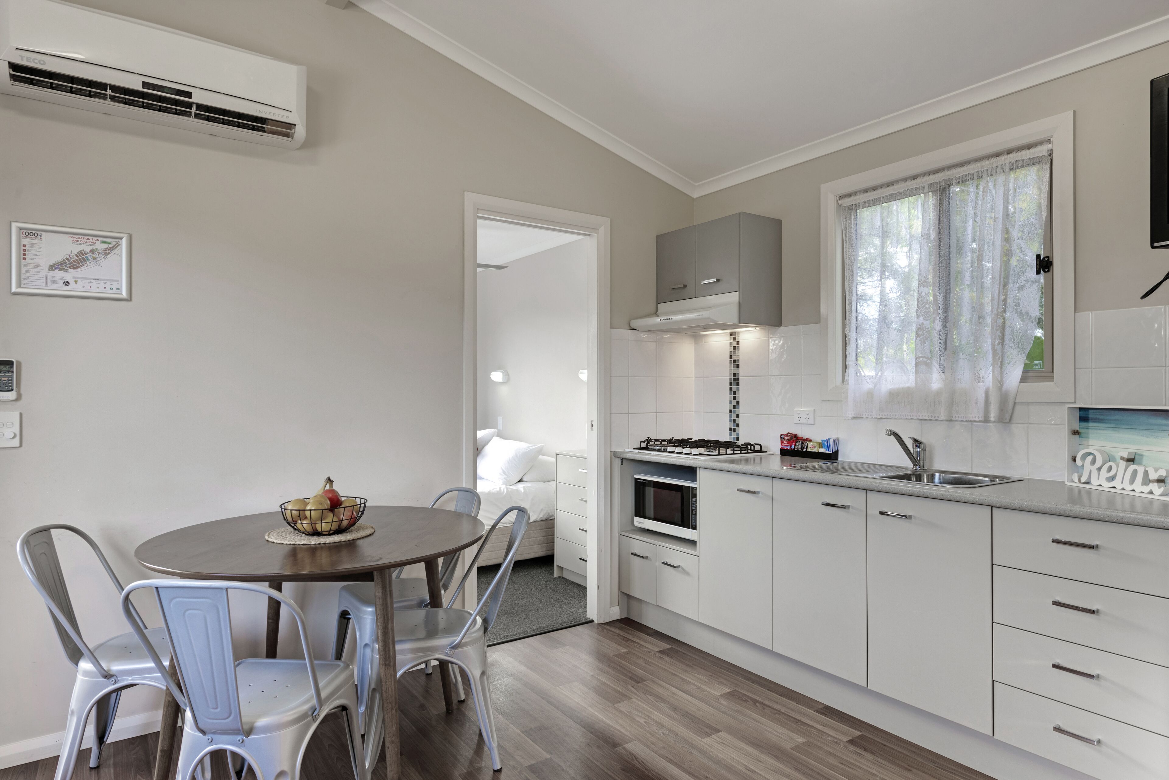 A modern kitchen with white cabinetry, a dining area with metal chairs, and a visible air conditioning unit.