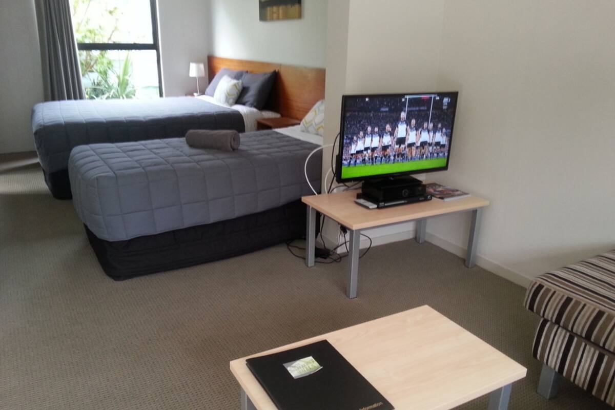 A hotel room with two beds, a TV, a desk, and a view of the outdoors.