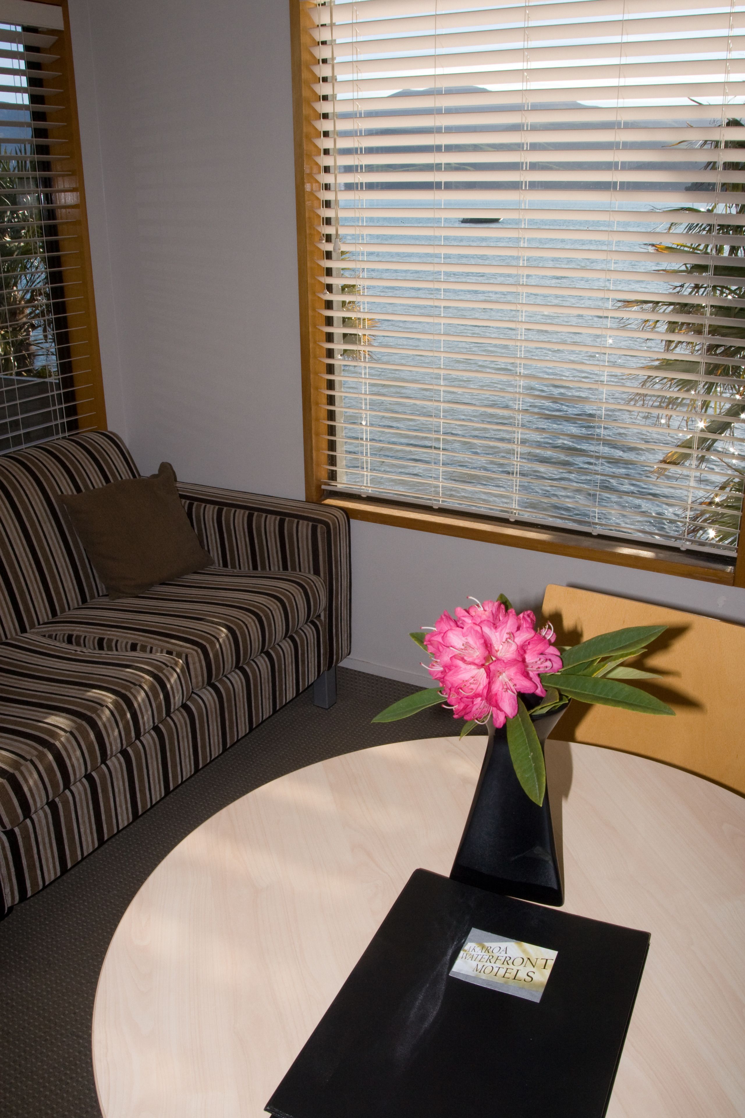A room with a striped sofa, a round table with a black base, and a vase with pink flowers.