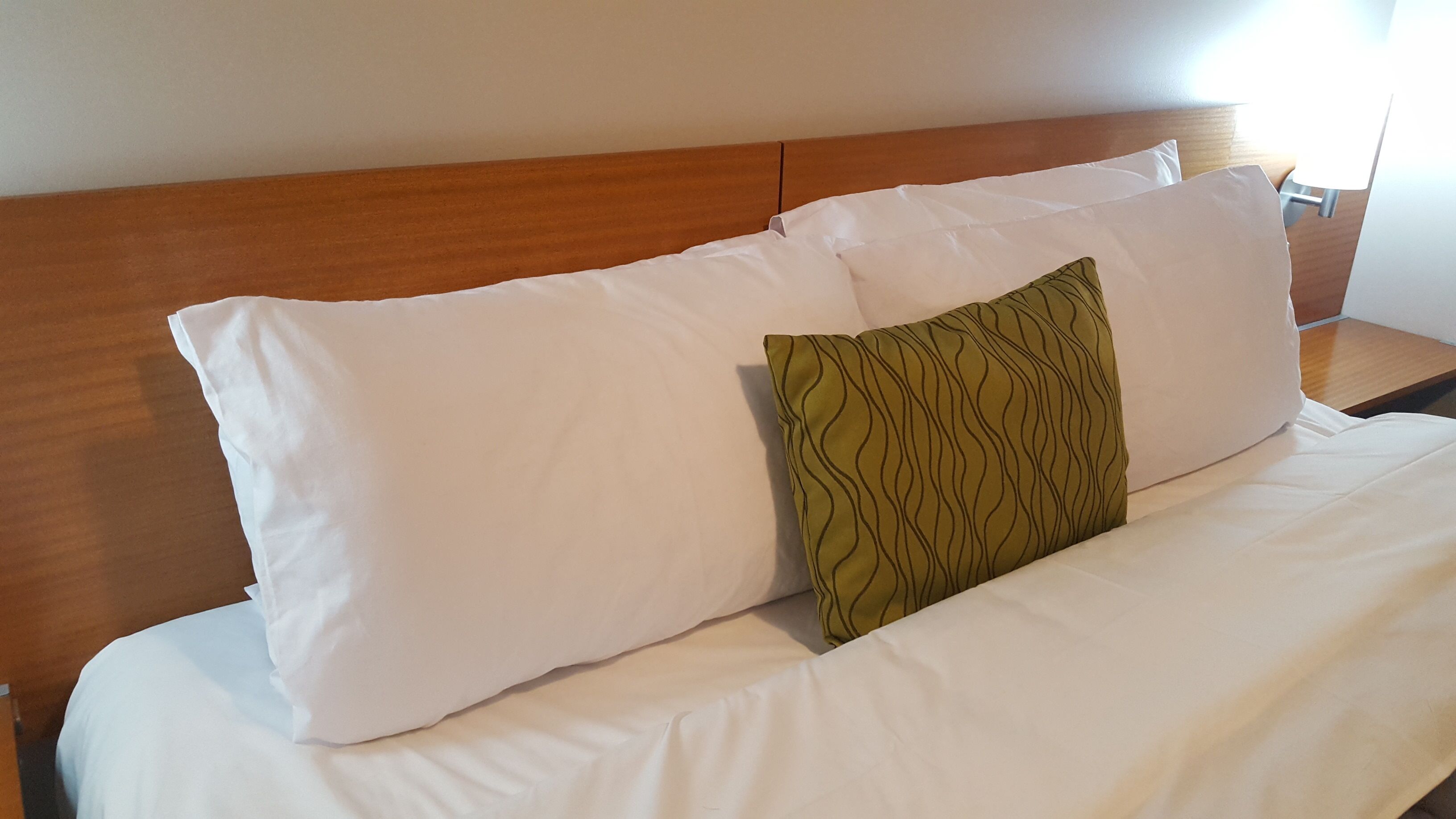 Ein Bett mit weißer Bettwäsche und einem einzelnen Kissen mit grünem Muster.