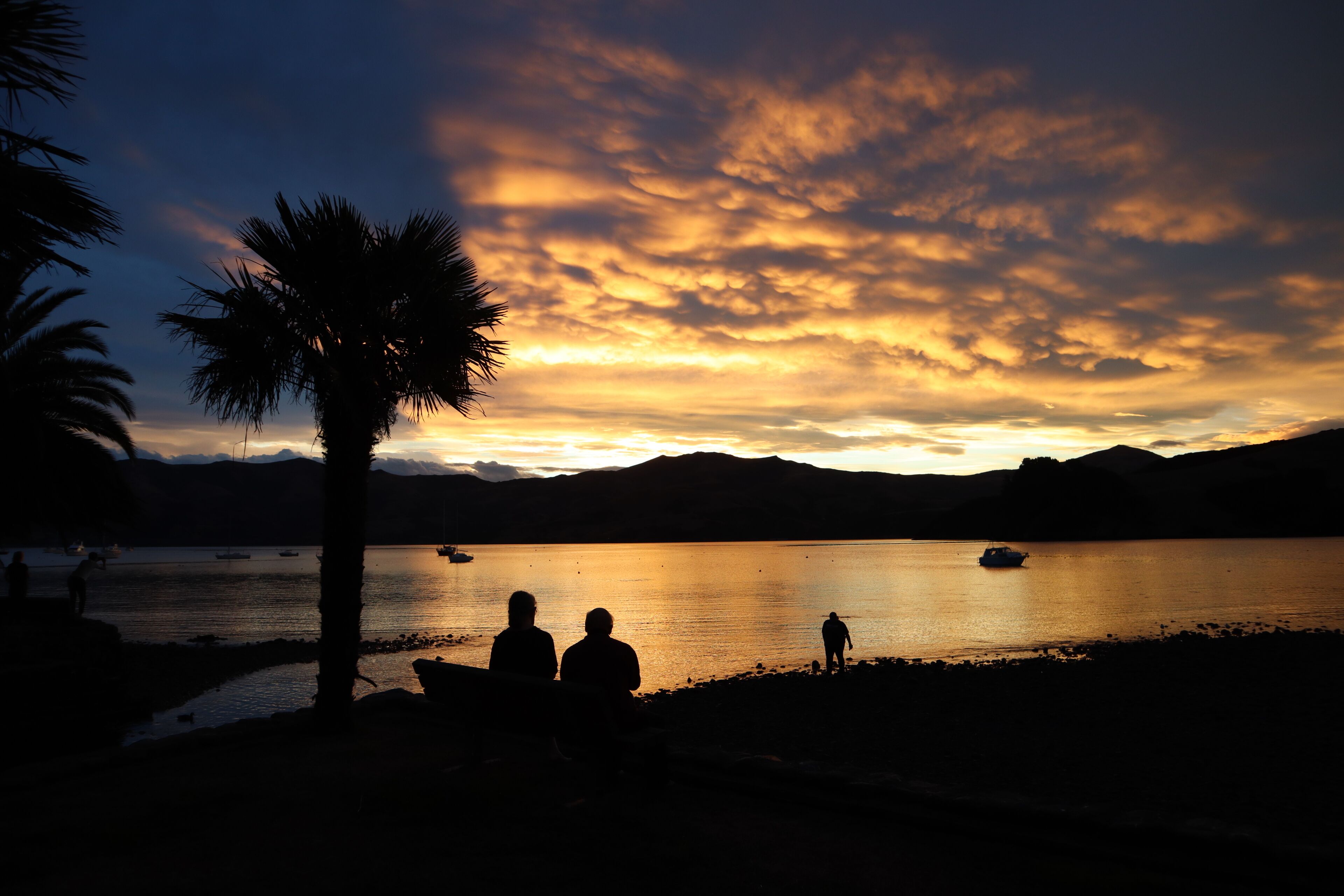 A sunset over a calm lake with silhouettes of people and boats.