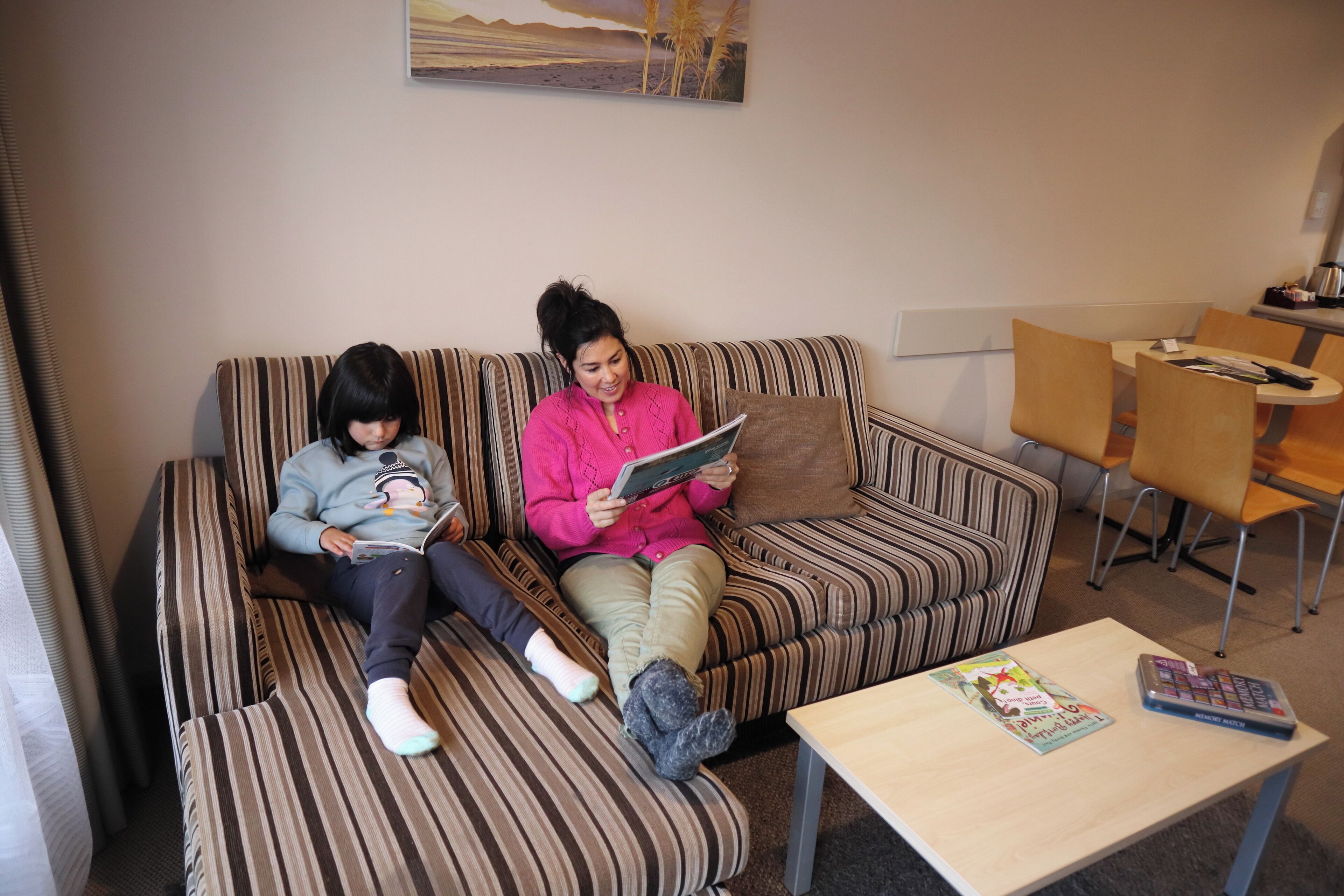 Un sofá a rayas con dos personas leyendo, una mesita con una revista y un cuadro en la pared.