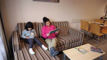 A striped sofa with two people reading, a small table with a magazine, and a painting on the wall.