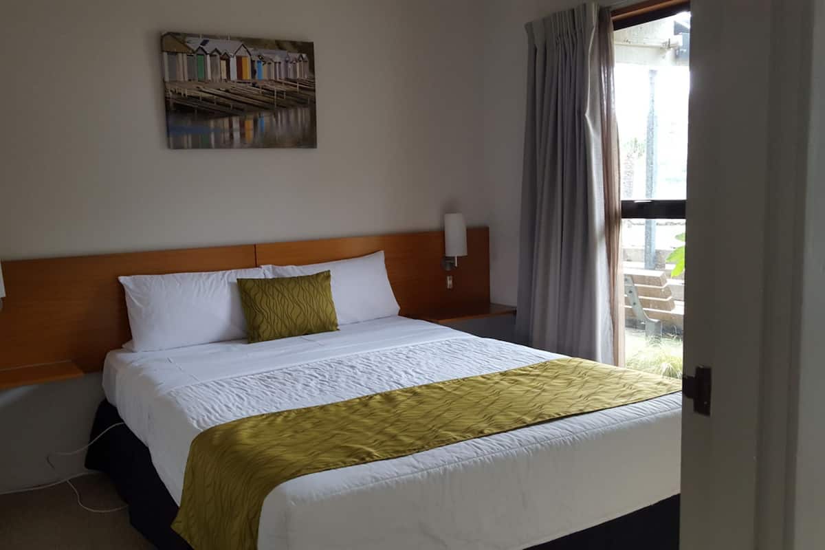 A hotel room with a bed, a headboard, a painting on the wall, and a window with curtains.