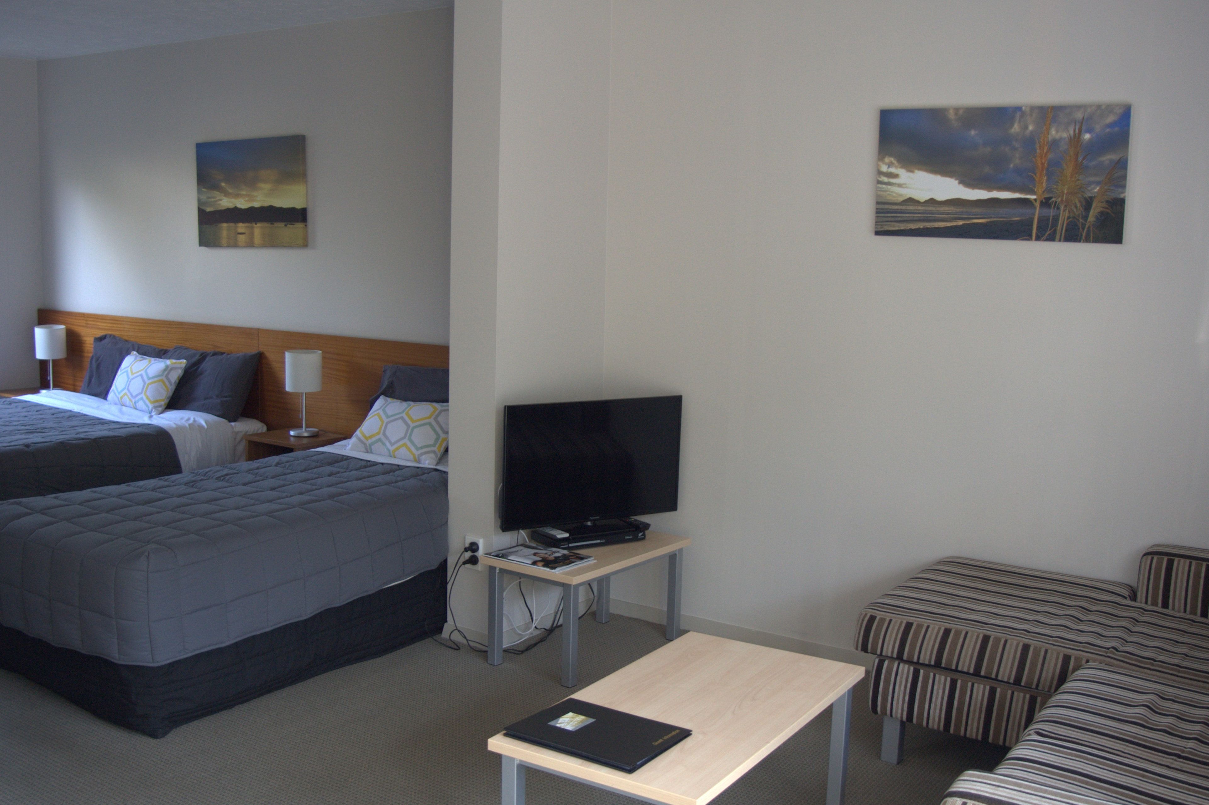 Habitación de hotel con dos camas, un televisor sobre una mesita y dos cuadros en las paredes.