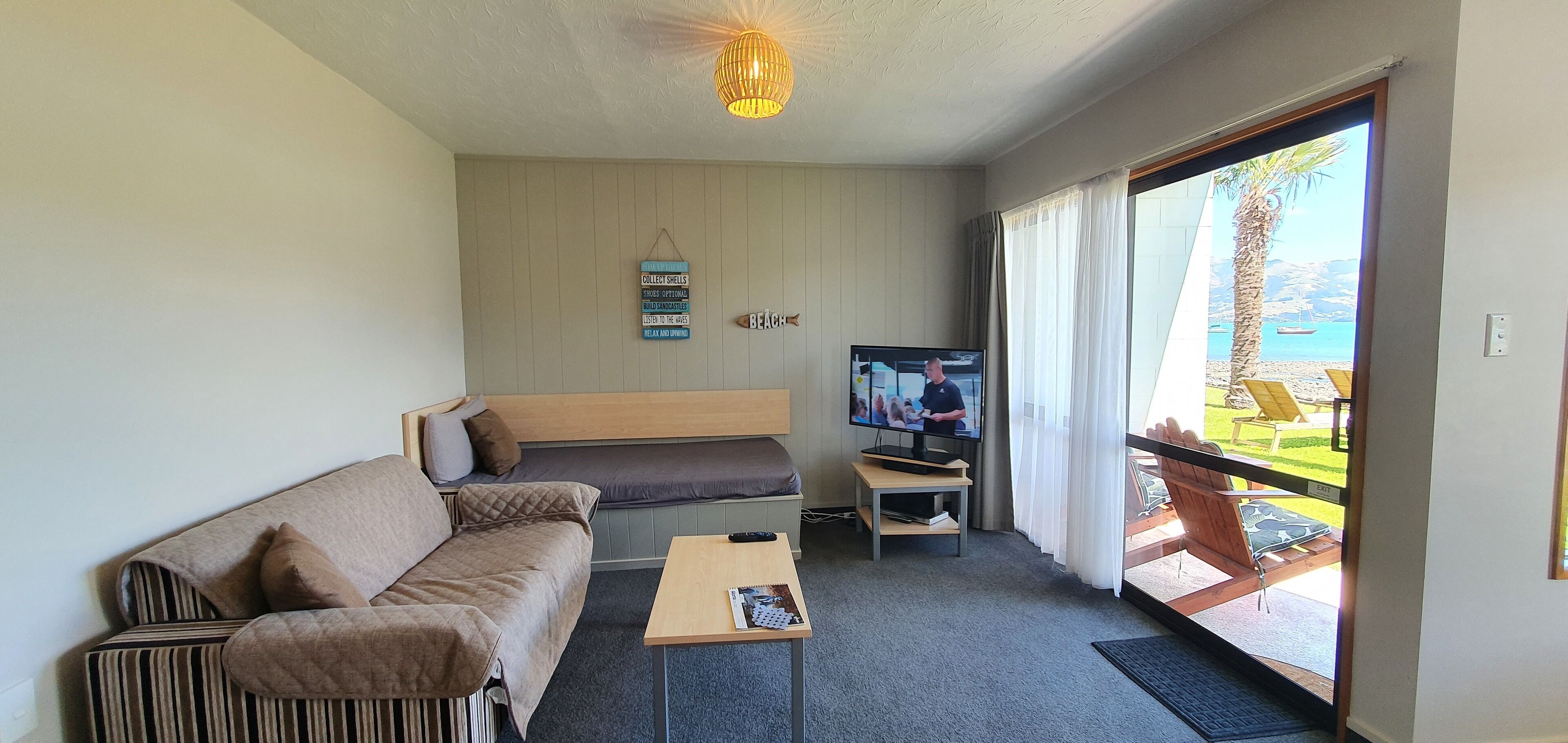 A room with a sofa, a small table, a TV, and a view of the beach.