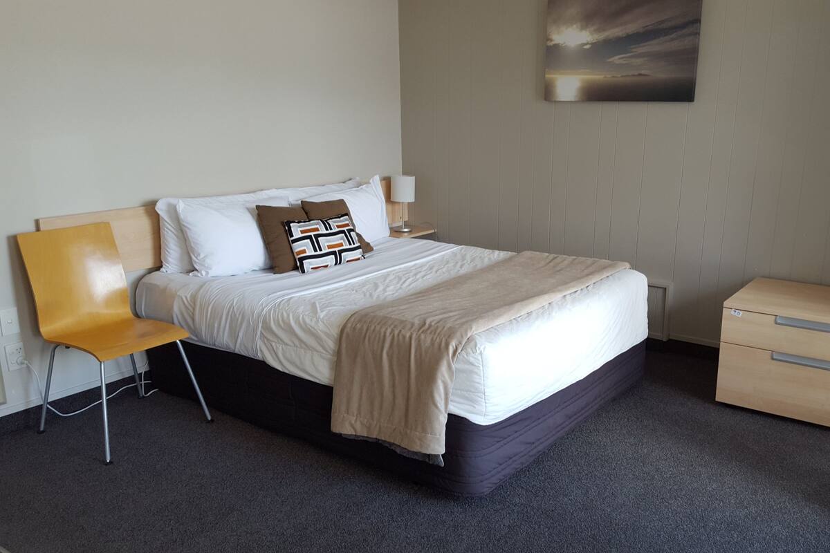 A neatly arranged hotel room with a bed, a chair, a bedside table, and a small cabinet.