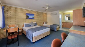 Une chambre d’hôtel avec un mur décoré d’un motif en briques, un lit recouvert d’une couverture bleue, un petit bureau avec une chaise, une table à manger et un coin cuisine.