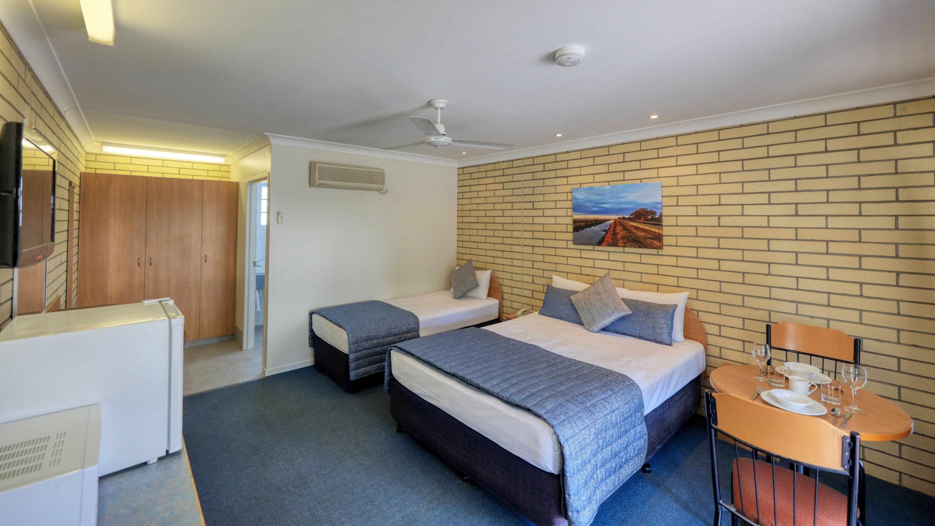 A hotel room with two beds, a dining area, a TV, and a brick wall.
