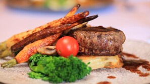 A plate of food with a steak, grilled vegetables, and a tomato.