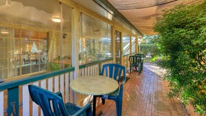 Une terrasse couverte avec une table ronde et des chaises, un sol en briques et une vue sur l’espace extérieur.