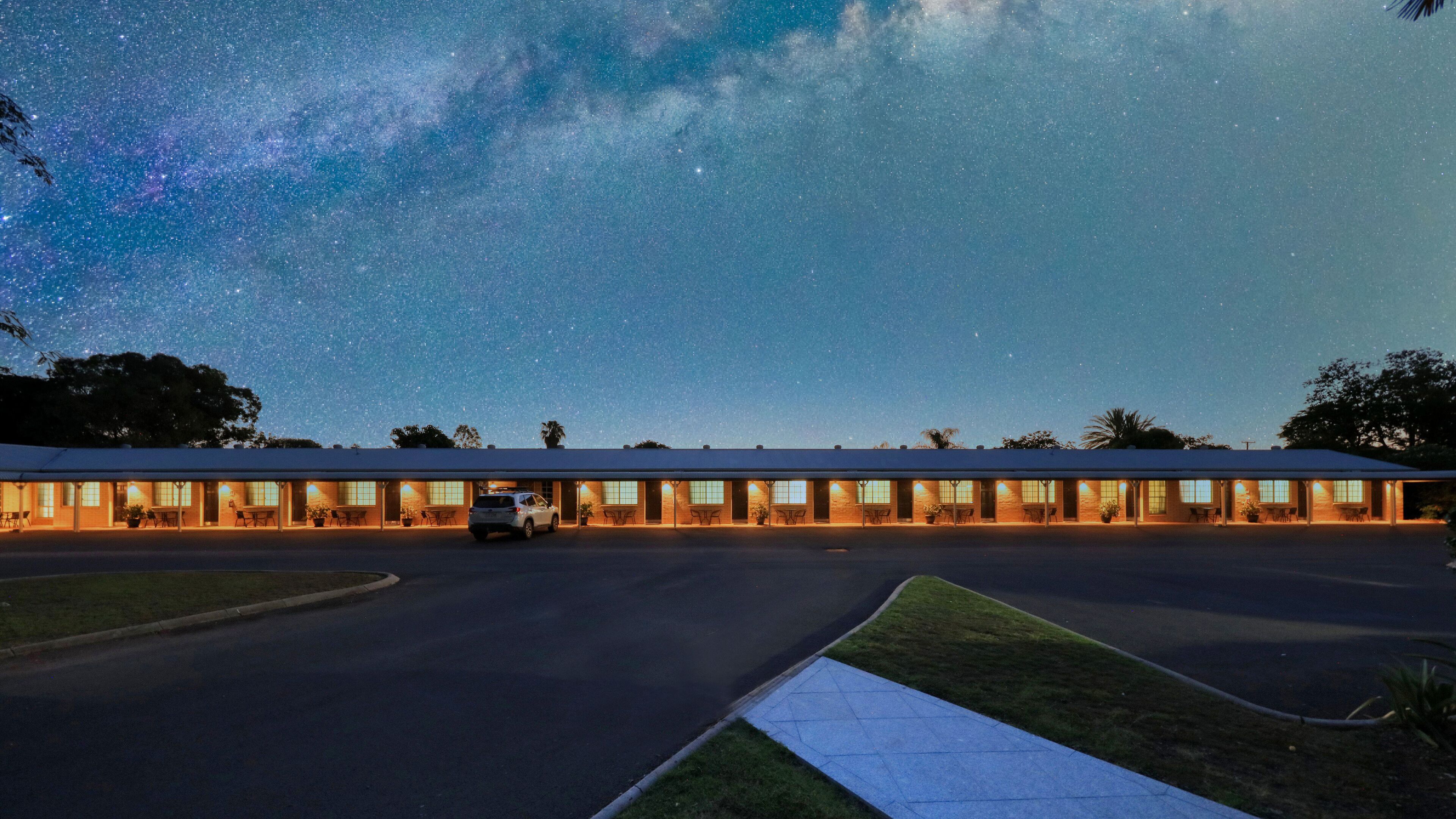 A motel with a row of rooms, a parking lot, and a clear night sky with stars.