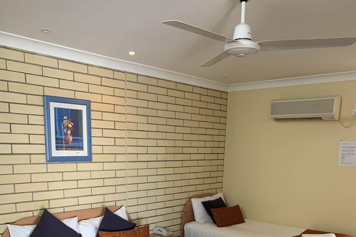 A hotel room with two beds, a ceiling fan, an air conditioning unit, and a framed picture on the wall.