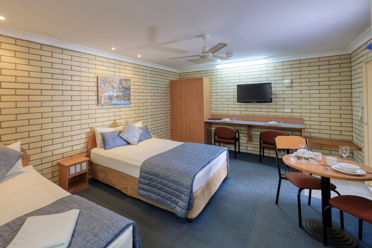 A hotel room with two beds, a desk, a chair, a television, and a ceiling fan.
