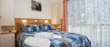 A hotel room with a large bed, a ceiling fan, a nightstand, and a window with sheer curtains.